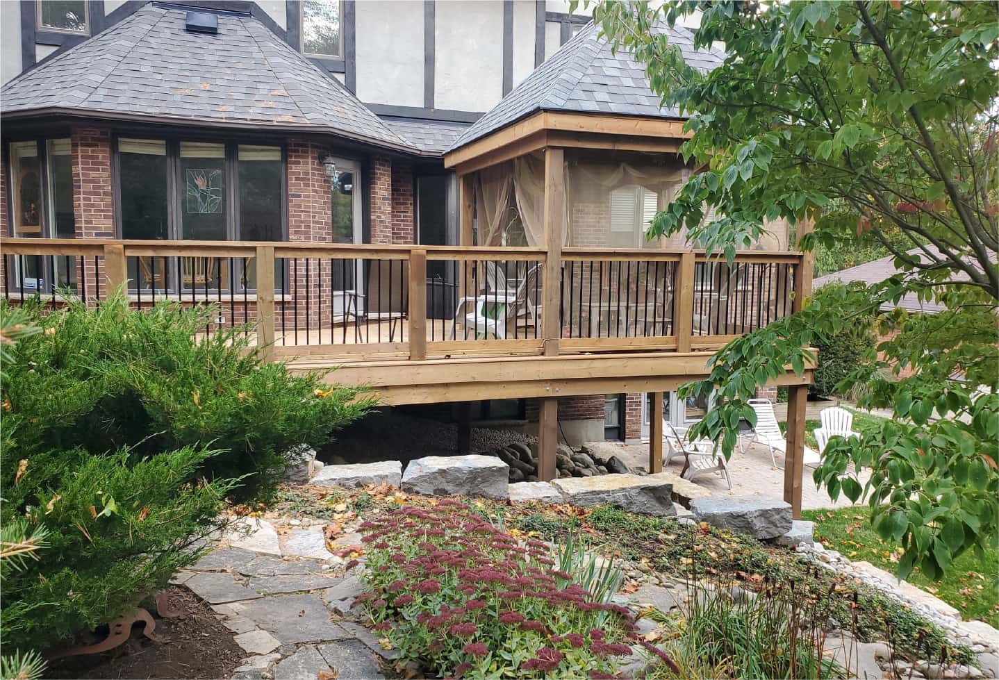 newly renovated wood deck with railing, bench and gazebo with deck chairs backyard trees