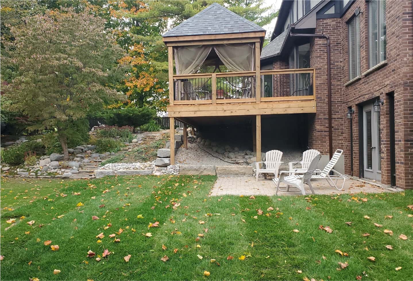 newly renovated wood deck with railing, bench and gazebo with deck chairs backyard trees and grass