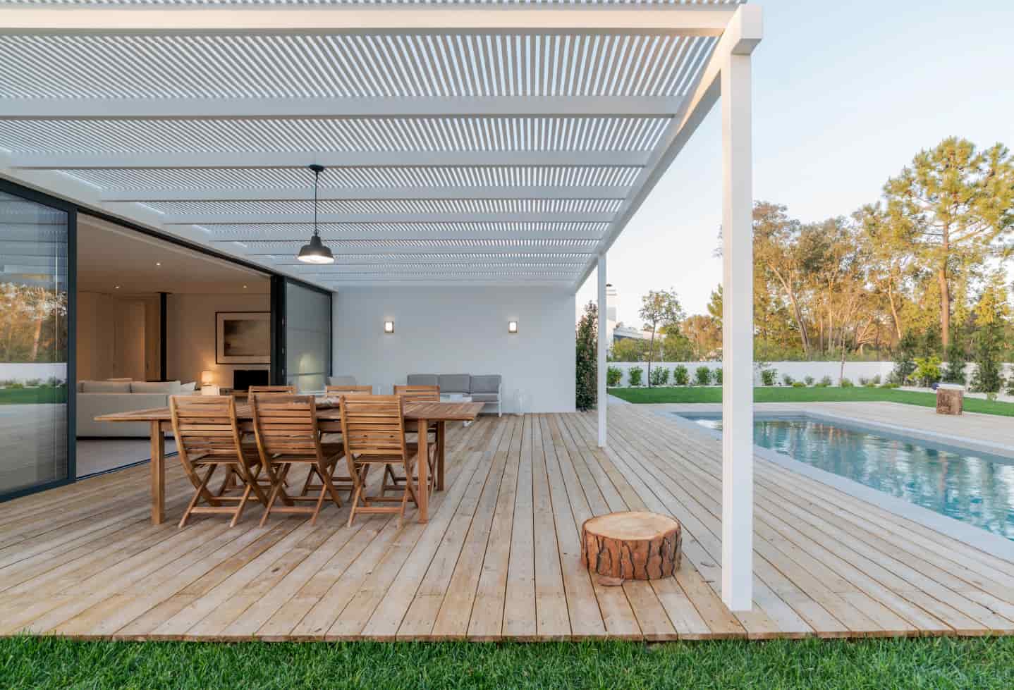 wood backyard patio with table and chairs next to swimming pool