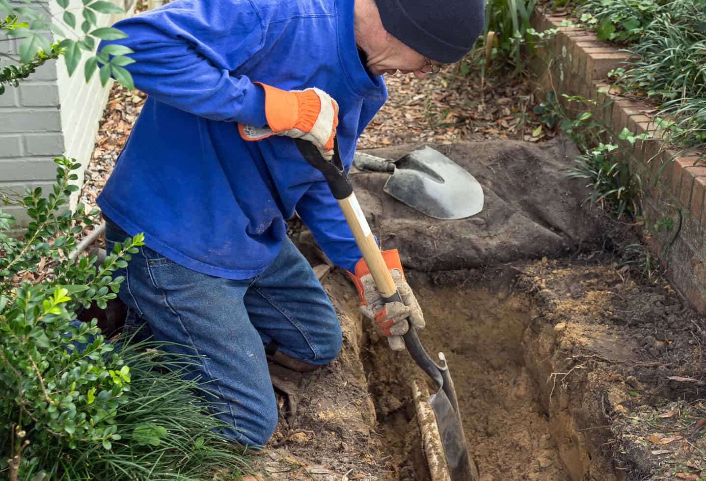 excavating done by man near house foundation with drainage pipes exposed