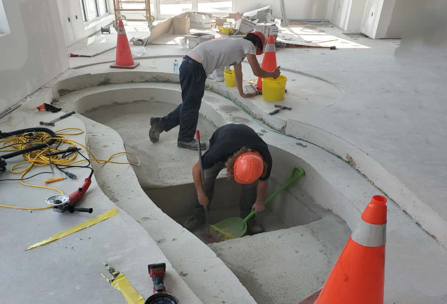 men working on the first step on pond installation indoors. hard hats cement floor with cement pond base