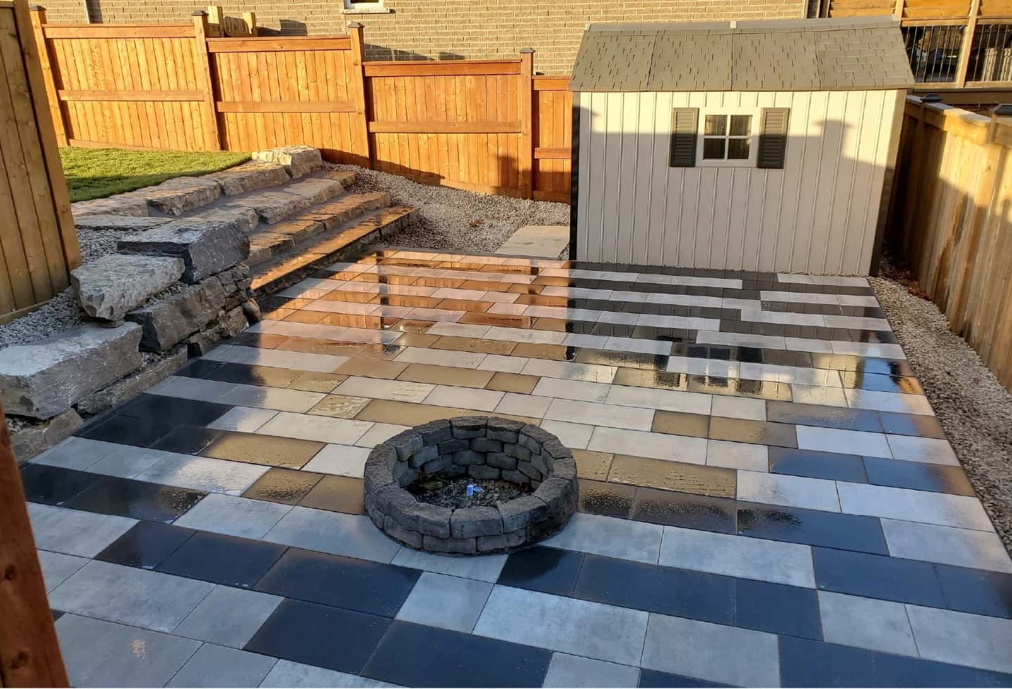 backyard black and stone tile patterned patio with grass in back with stone steps and shed